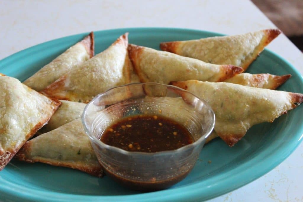 Close up of finished spicy krab wontons with sweet mustard sauce on a turquoise plate