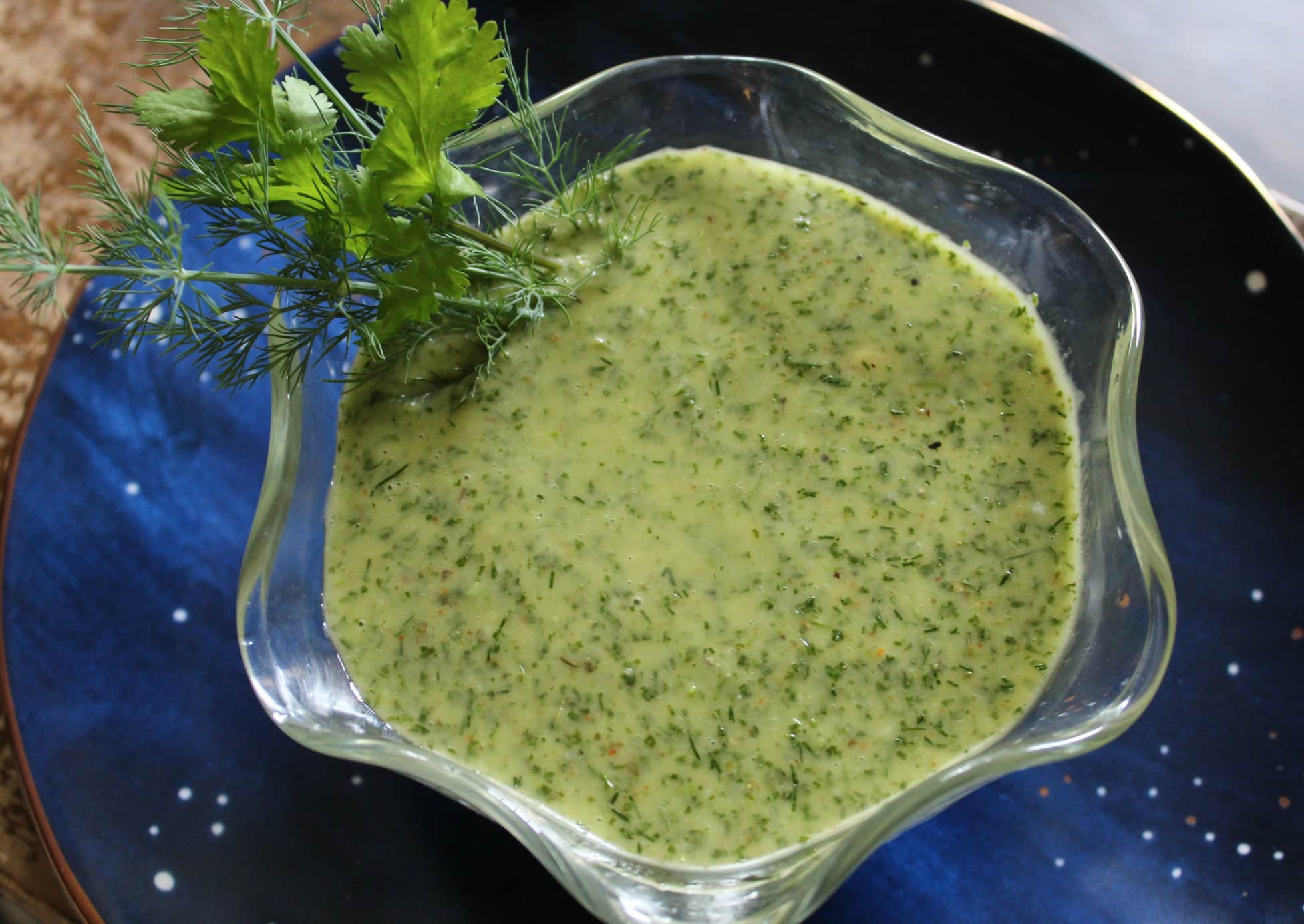 Cilantro dill lemon salad dressing in a clear bowl on a blue plate