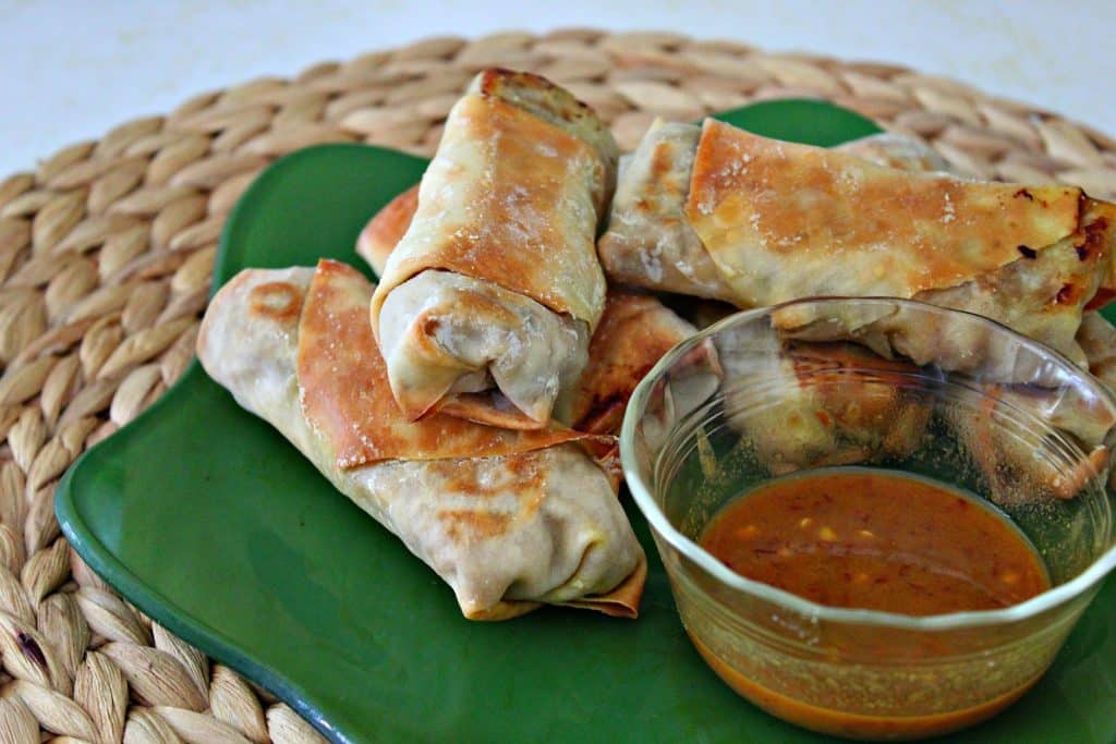 baked shrimp egg rolls on a green plate with sauce on a woven place mat