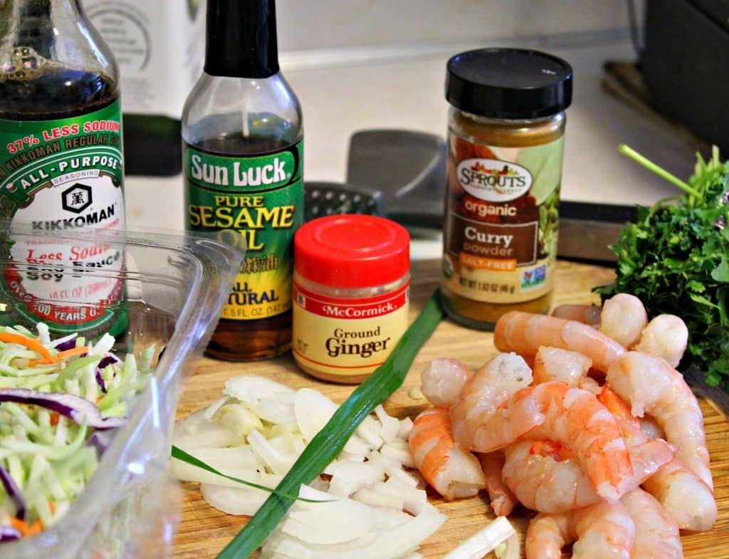 shrimp egg roll ingredients, soy sauce sesame oil curry ginger broccoli slaw shrimp onion on a bamboo cutting board