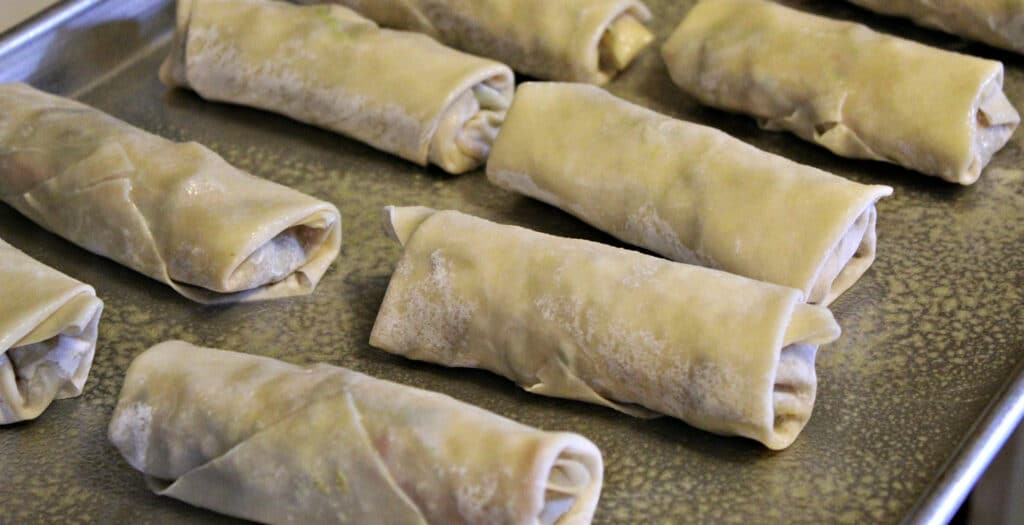 unbaked egg rolls on a greased cookie sheet