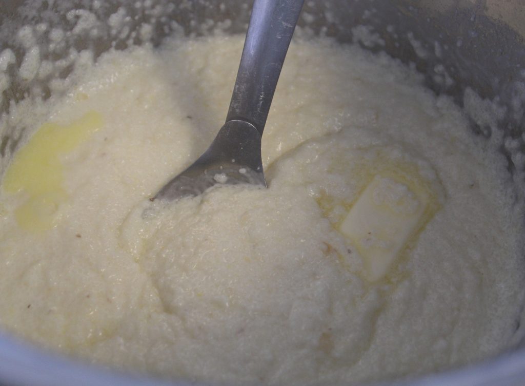 Plain Grits cooked with cream and butter in a pan with a stir spoon