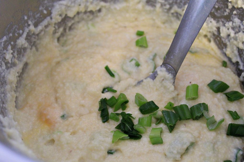 White grits in a pan with melted cheese and green onions