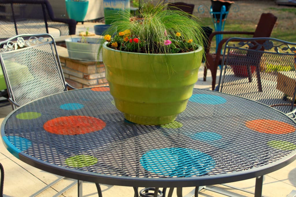 Finished wrought iron redone table on the back patio with a green planter and grass and flowers in it.