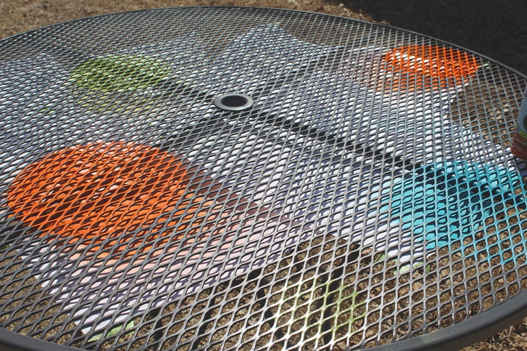 Beginning to spray stencils on table with orange blue and green paint on a grey table