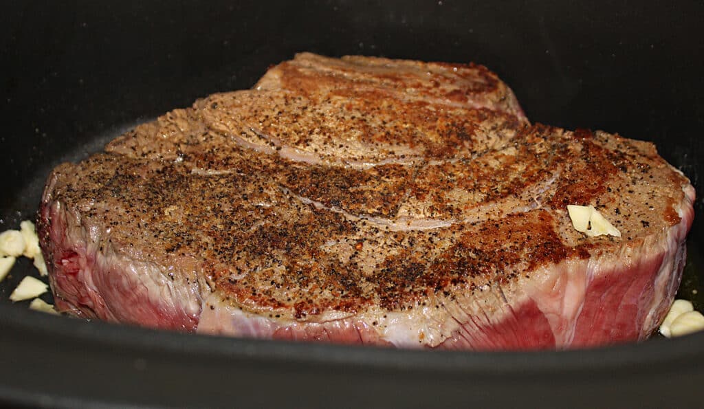 Seared chuck roast in a crock pot with onions and garlic.