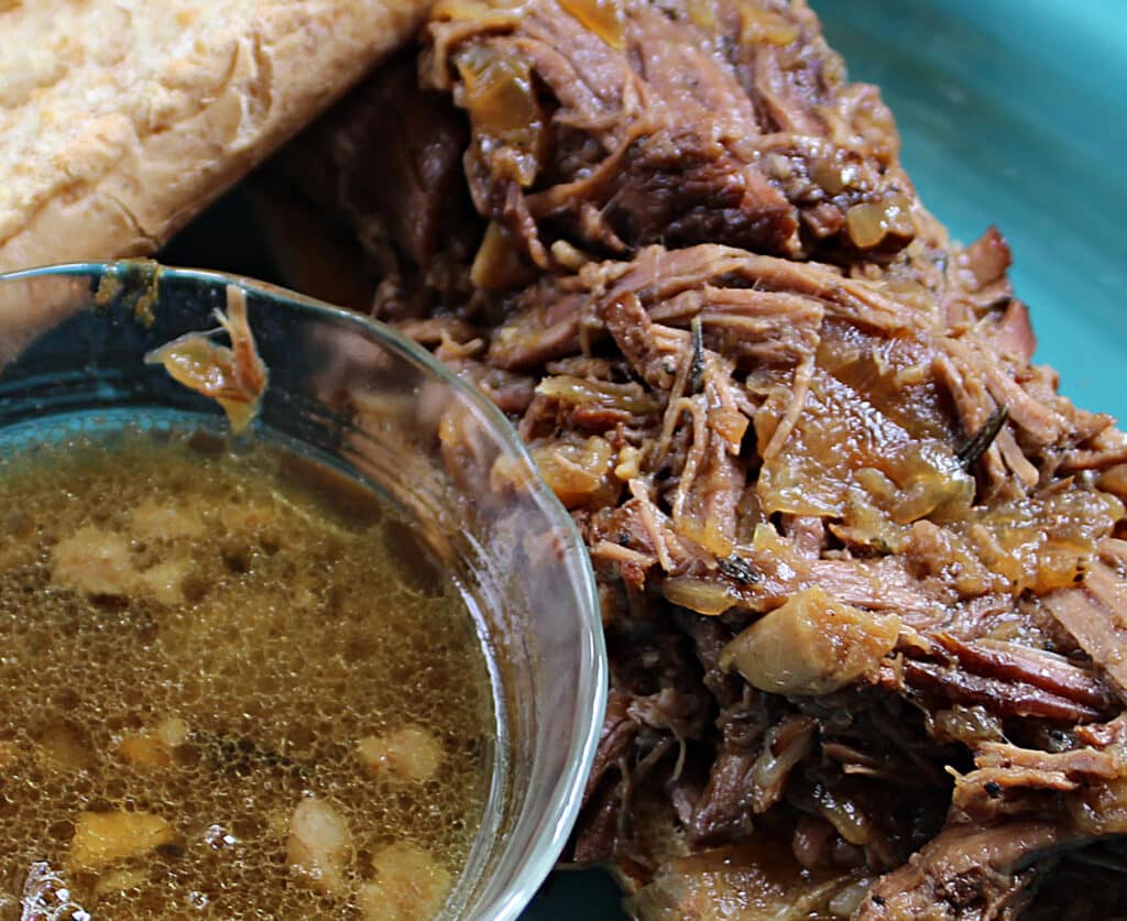 Savory shredded beef with cooked onions and garlic next to a bowl of au jus.