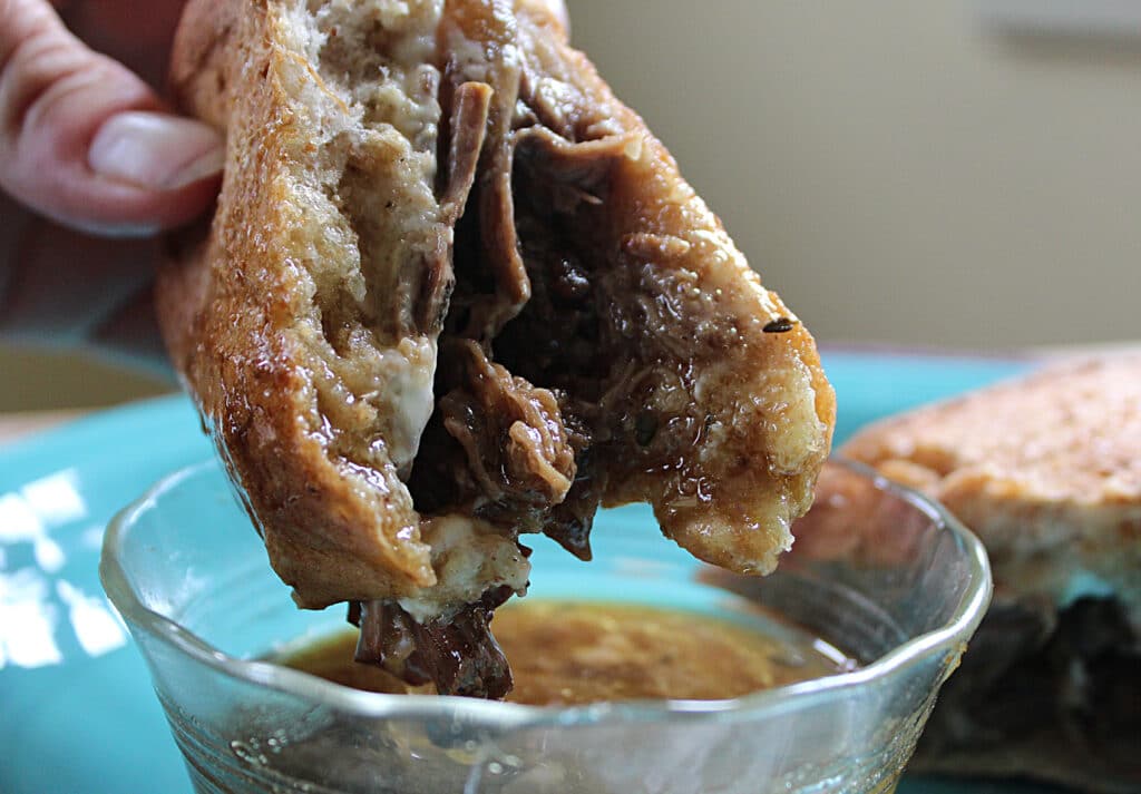 half of a drip beef sandwich dunked in homemade au jus