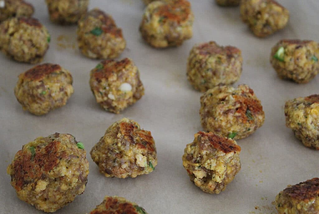 partially cooked sausage balls on a cookie tray with parchment paper