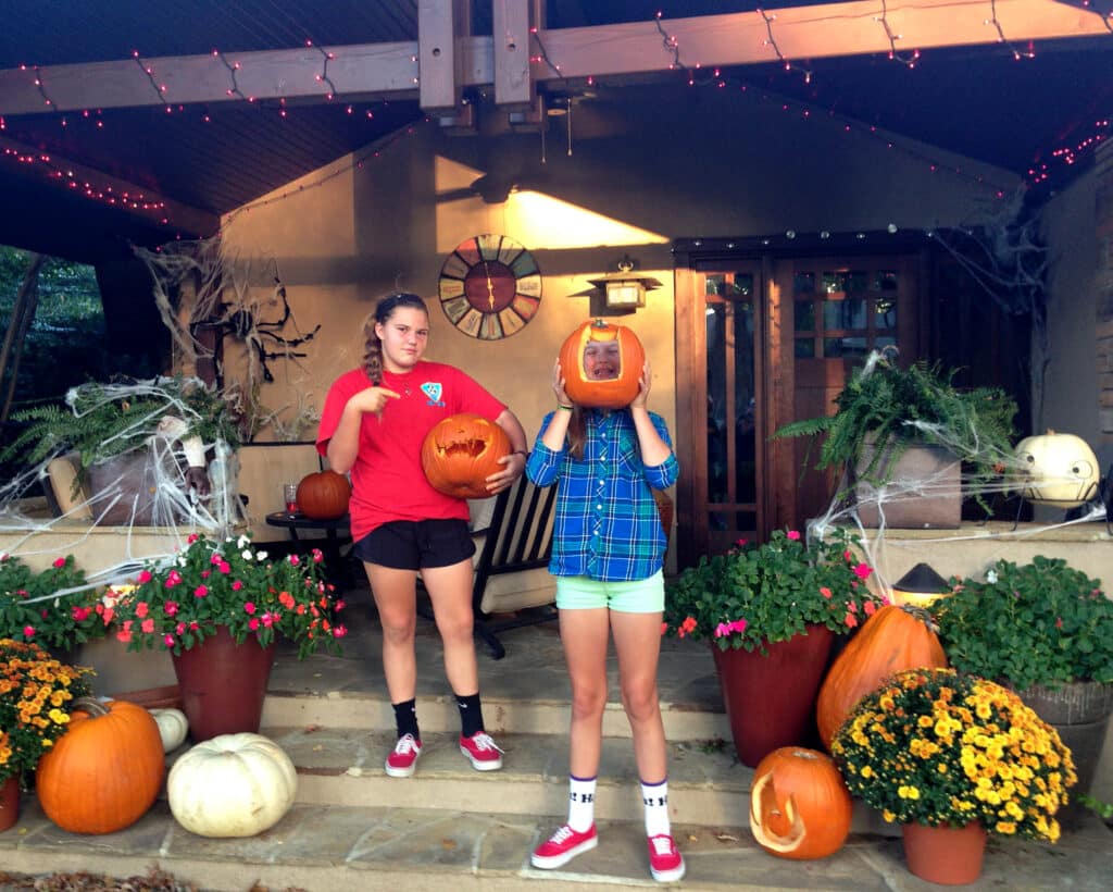 kids carving pumpkins on front decorated porch before halloween