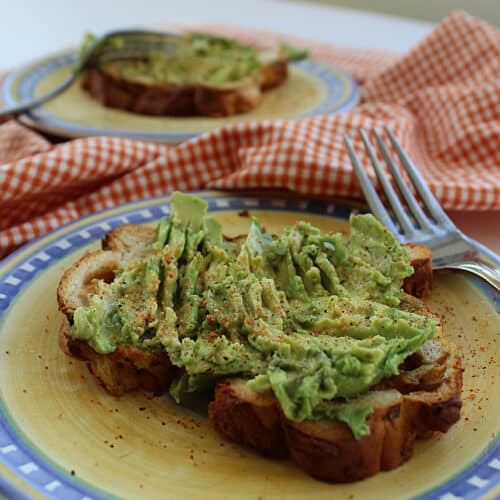 2 spicy avocado toasts on plates with forks