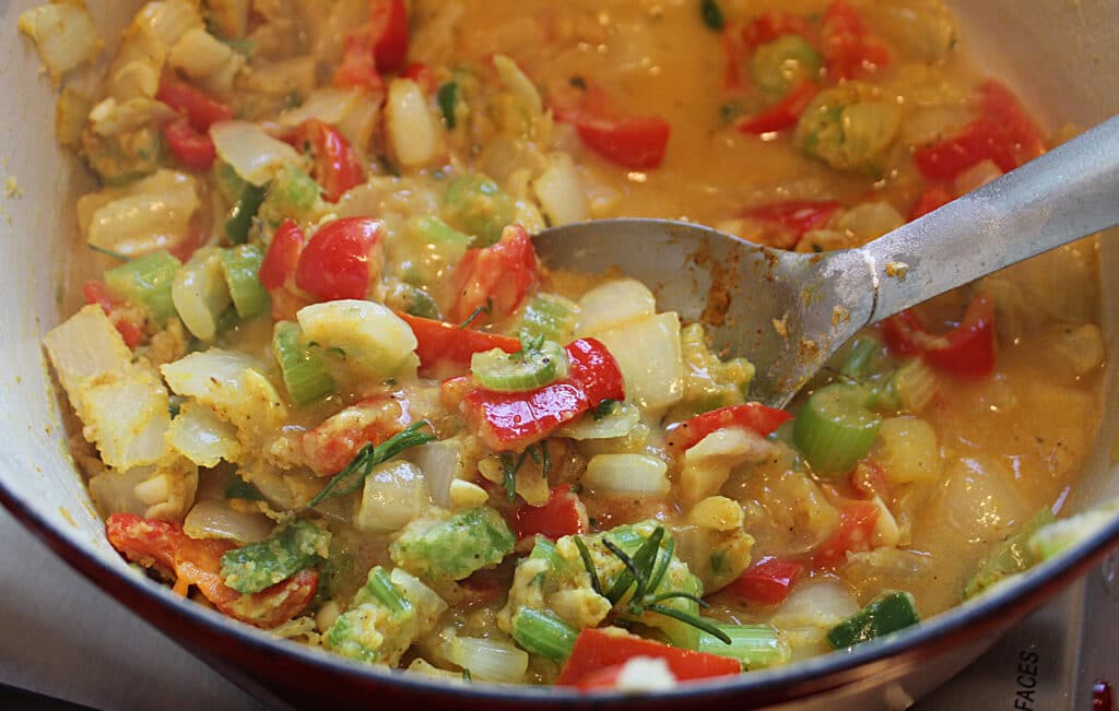 Onions, celery, red pepper, jalapeno, garlic with seasonings and flour being stirred in a dutch oven.