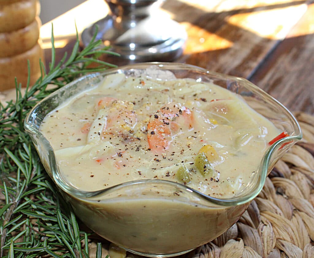 Seafood chowder in a glass bowl with rosemary leaves ready to serve.