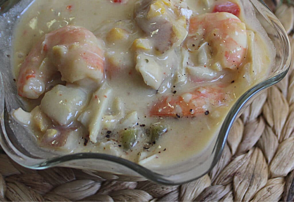 close up of seafood chowder in a glass bowl on a woven place mat