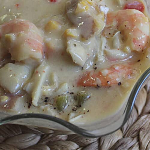 close up of seafood chowder in a glass bowl on a woven place mat