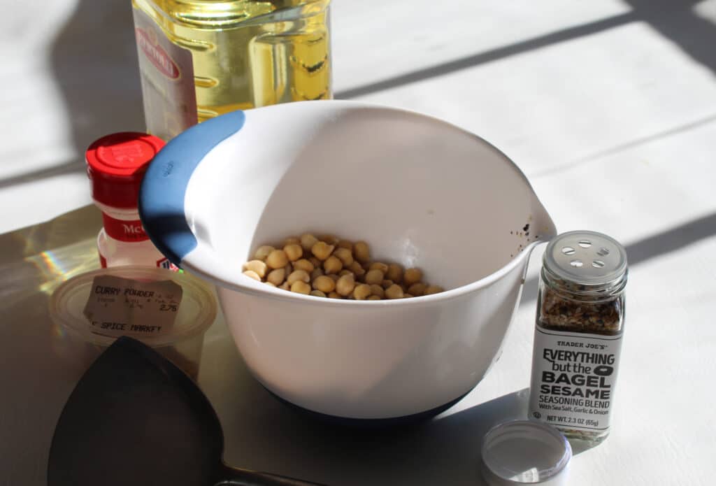 plain chickpeas in a white bowl with curry, garlic salt, everything seasoning, olive oil