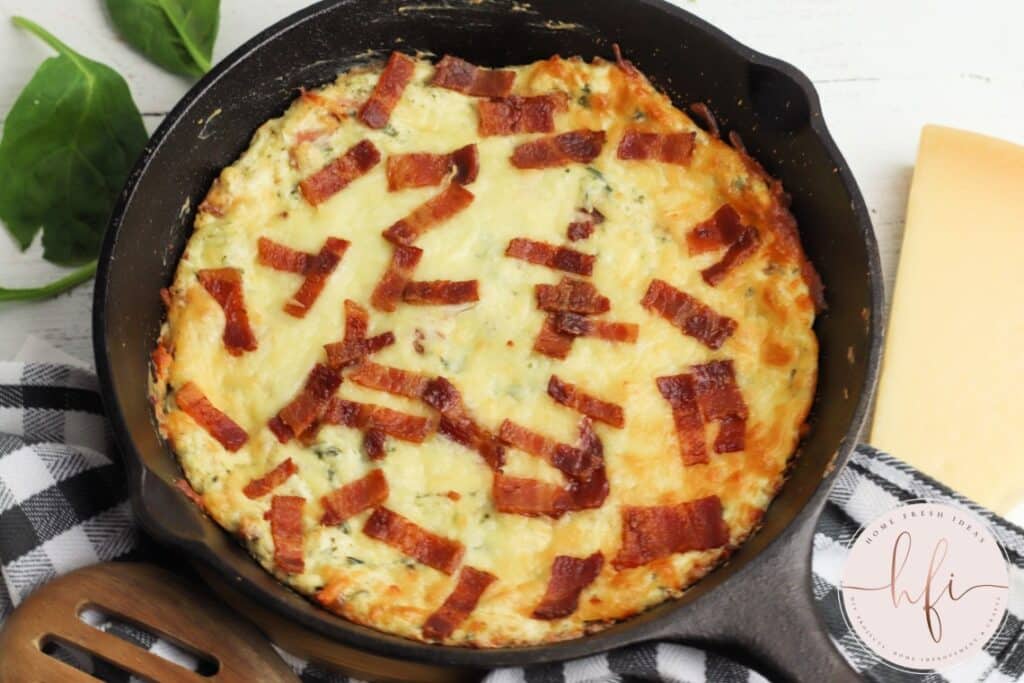 Warm Bacon Cream Cheese Dip in a cast iron skillet on a black and white kitchen towel