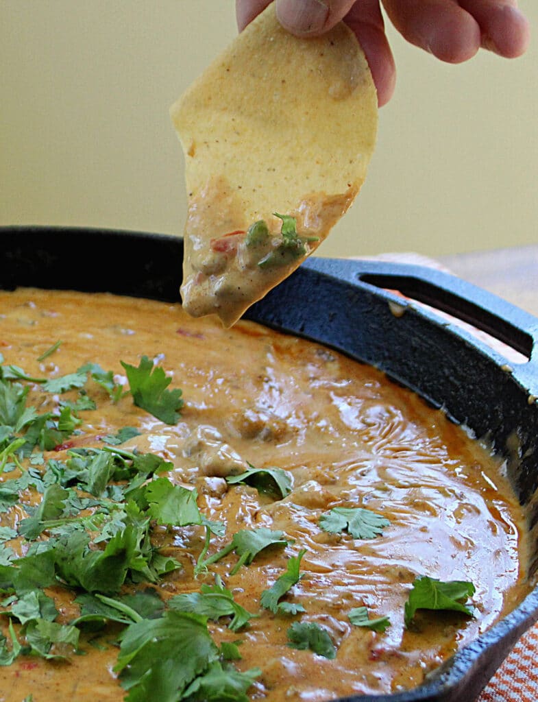 Spicy Sausage Rotel Cheese Dip in a cast iron skillet with dip on a chip