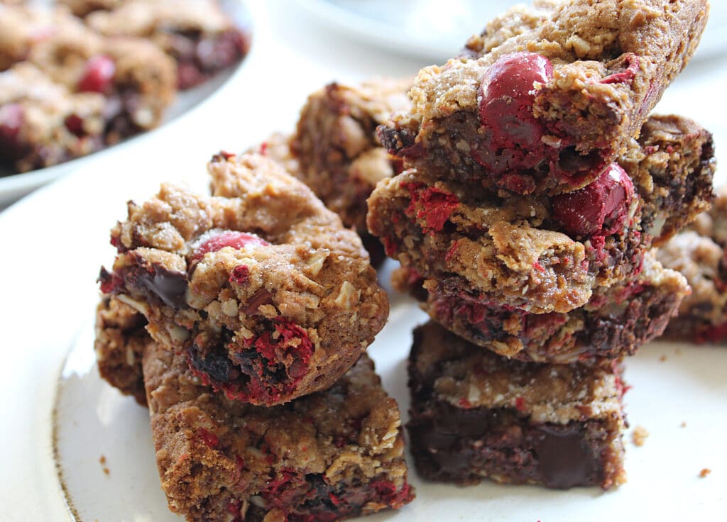 Close up of stacked chocolate chunk chocolate covered cherry bars stacked to show side view of cooked bars on a white plate