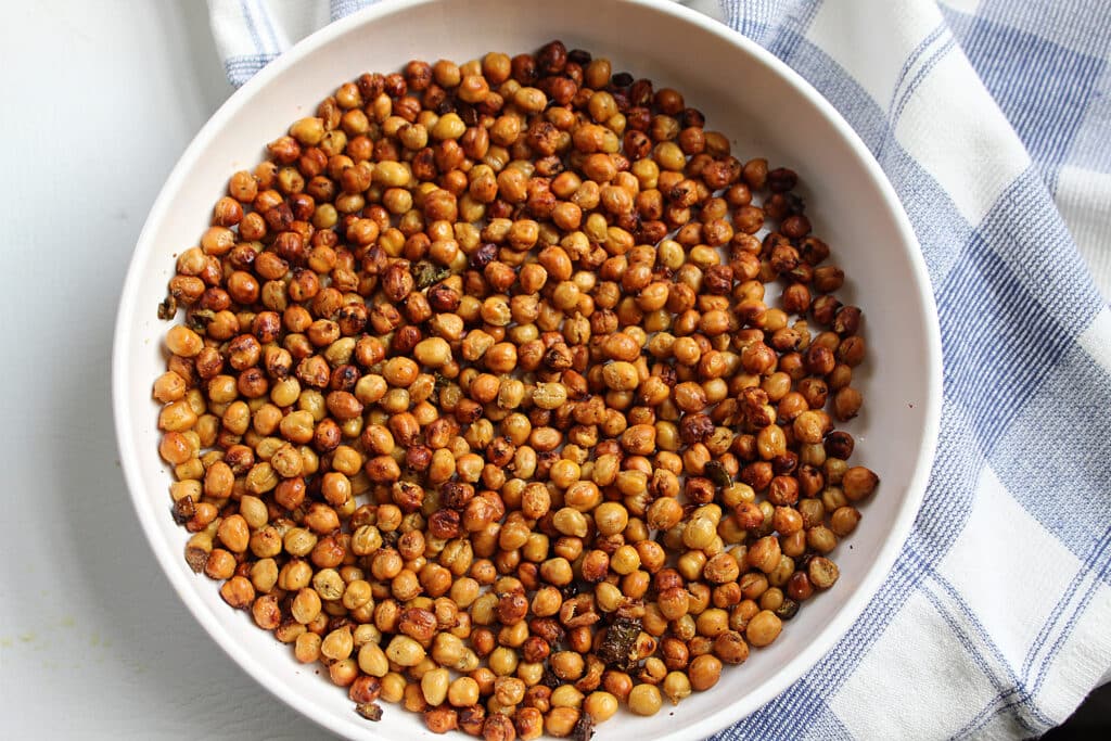 overhead shot of finished spicy roasted chickpeas with jalapenos in a white bowl with a blue and white towel.