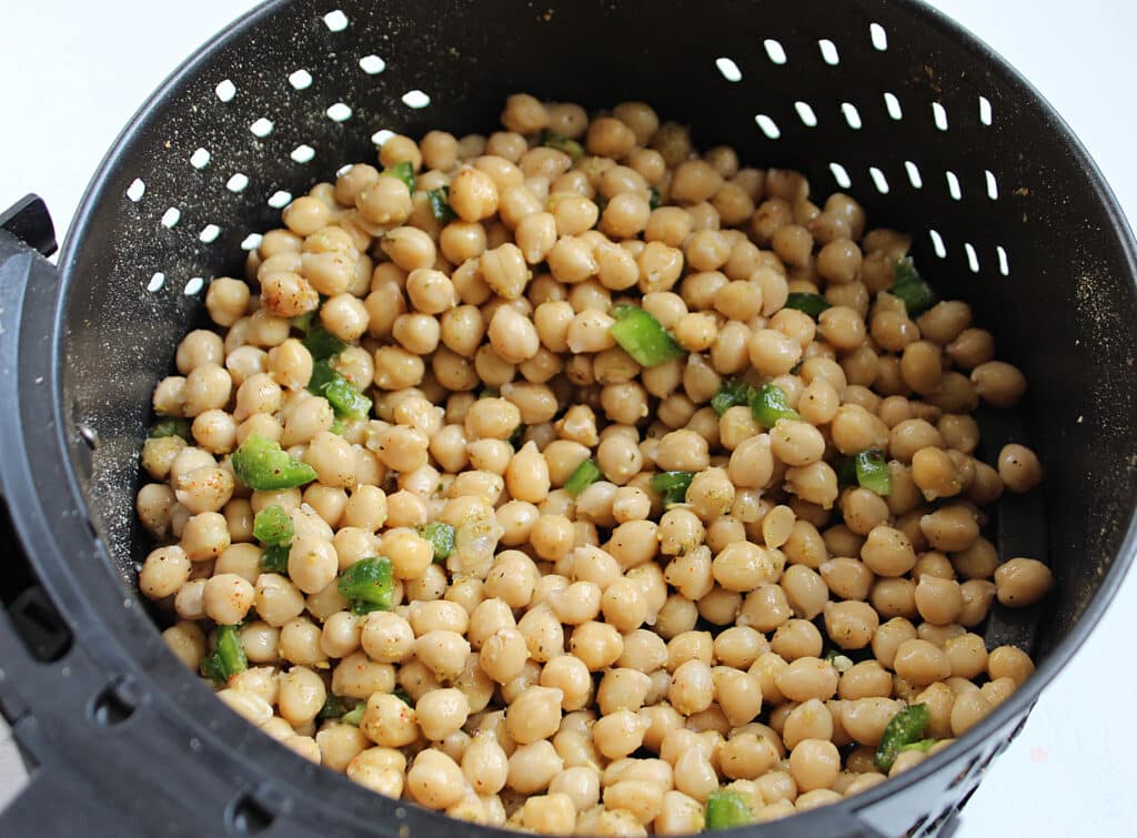 Canned chickpeas with chopped jalapeno in an air fryer basket before cooking.