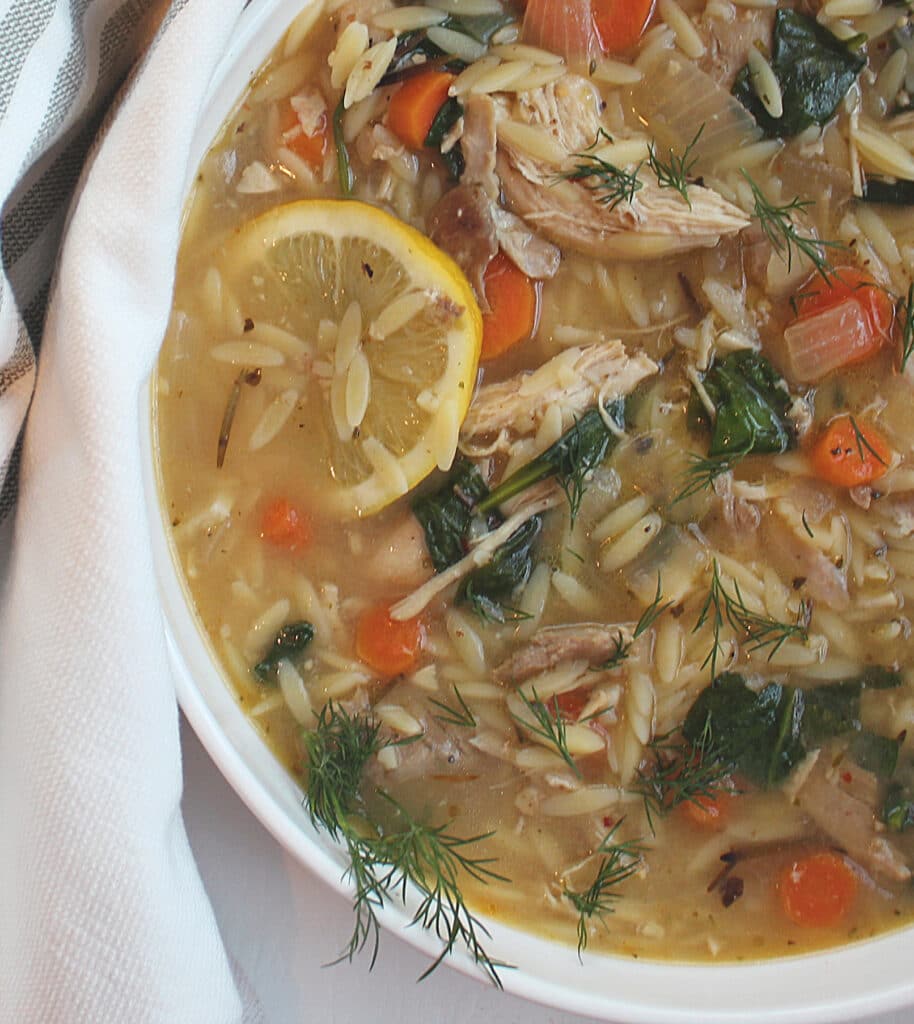 Bowl of Lemon Chicken Orzo Soup with lemon wedge in a white bowl