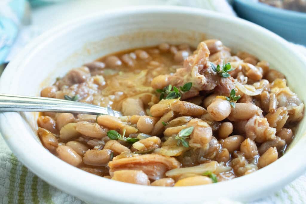 Pinto beans and ham with fresh herbs on top in a white individual bowl.