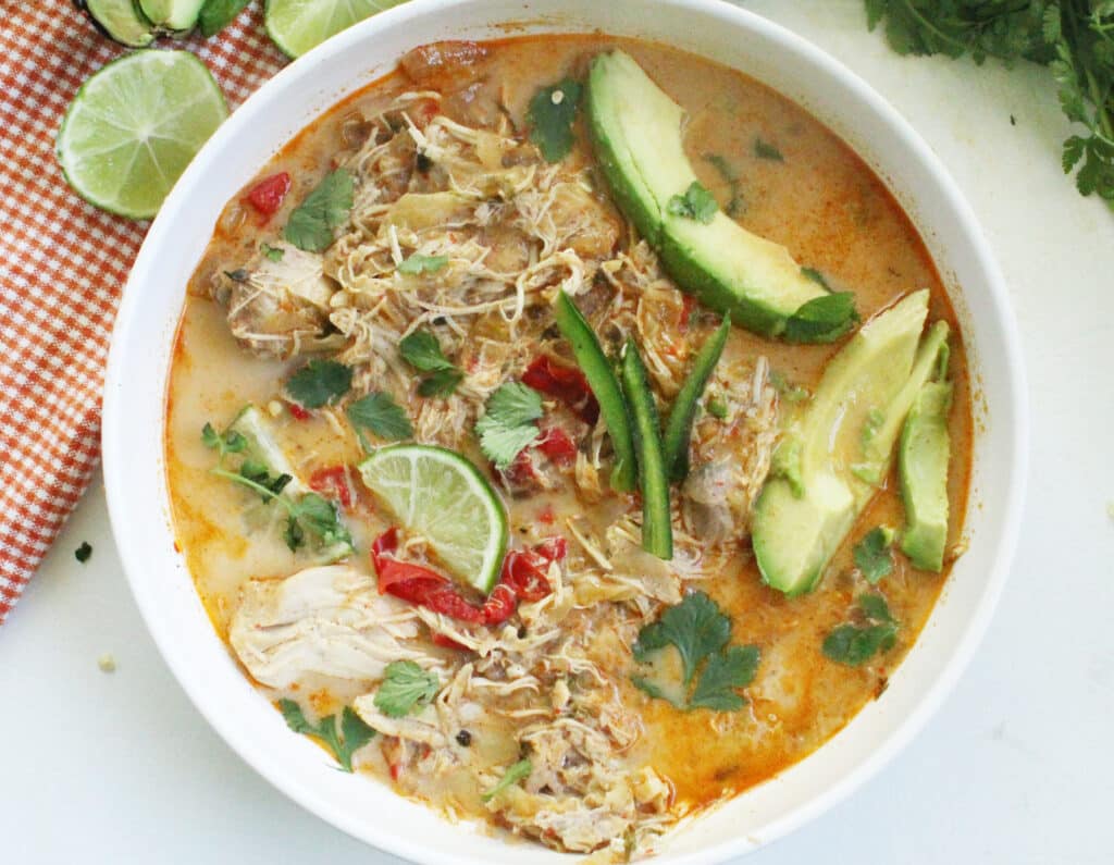 overhead photo of low carb mexican chicken soup in a white bowl with avocado and lime slimes