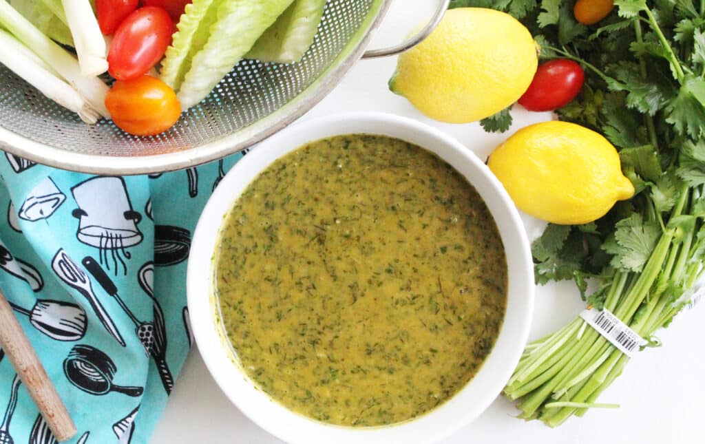 overhead picture of cilantro dill dressing with lettuce tomatoes onions lemons and cilantro on the side.