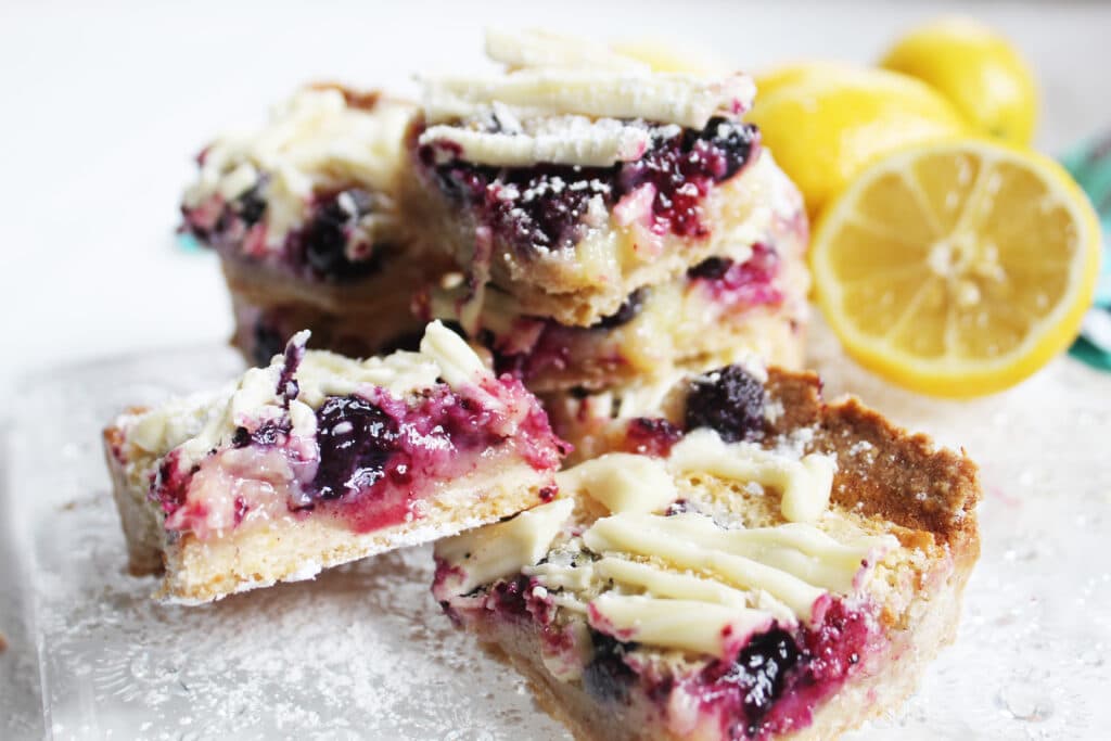 individual and stacks of white chocolate blueberry lemon bars on a crystal plate