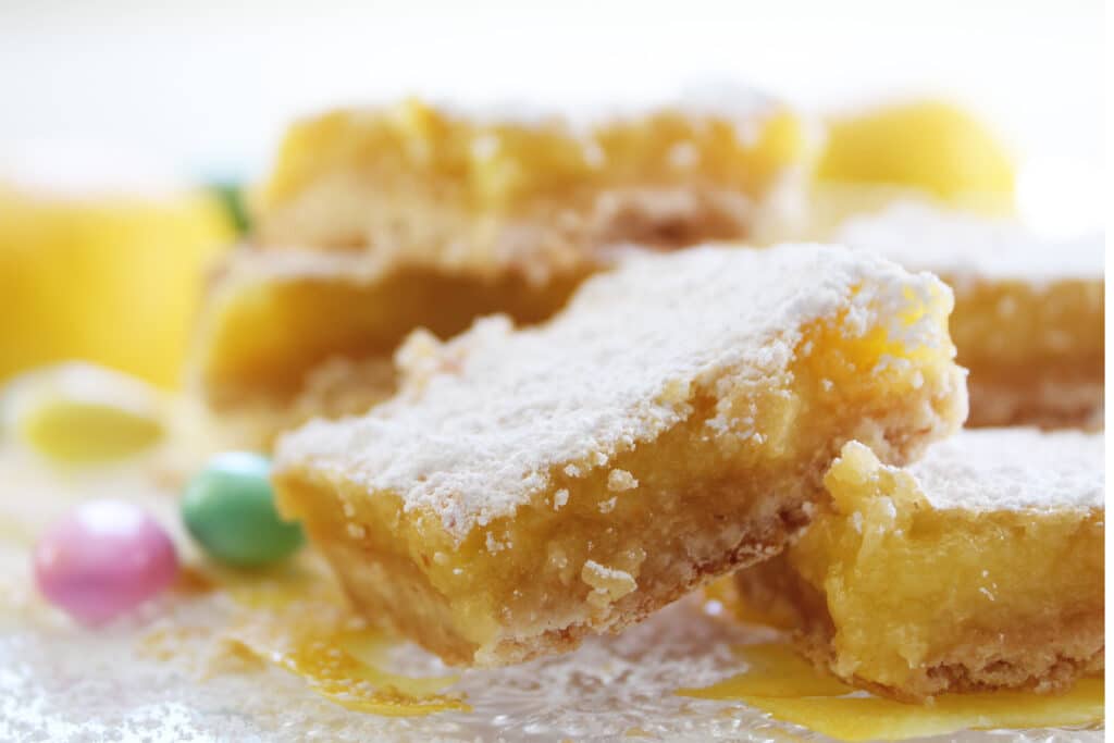 Close up of lemon bars with powdered sugar and jordan almonds on a crystal plate.