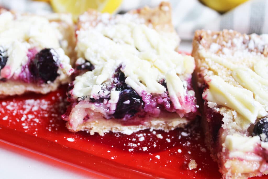 close up of white chocolate blueberry lemon bars on an orange polka dot glass serving tray