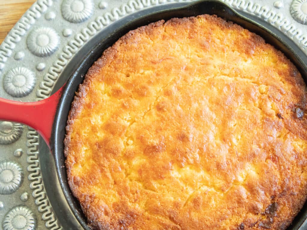 overhead picture of golden cast iron skillet cornbread in a red cast iron skillet on a silver  platter