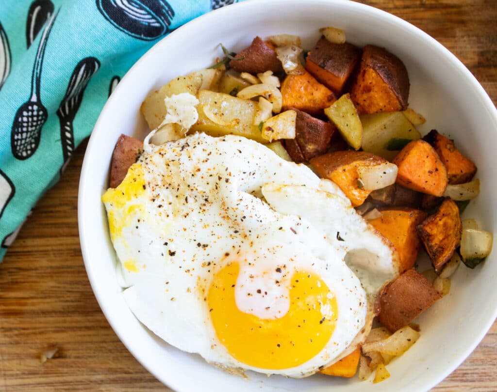 Sweet potato hash with a fried egg on a butcher block and a teal towel.