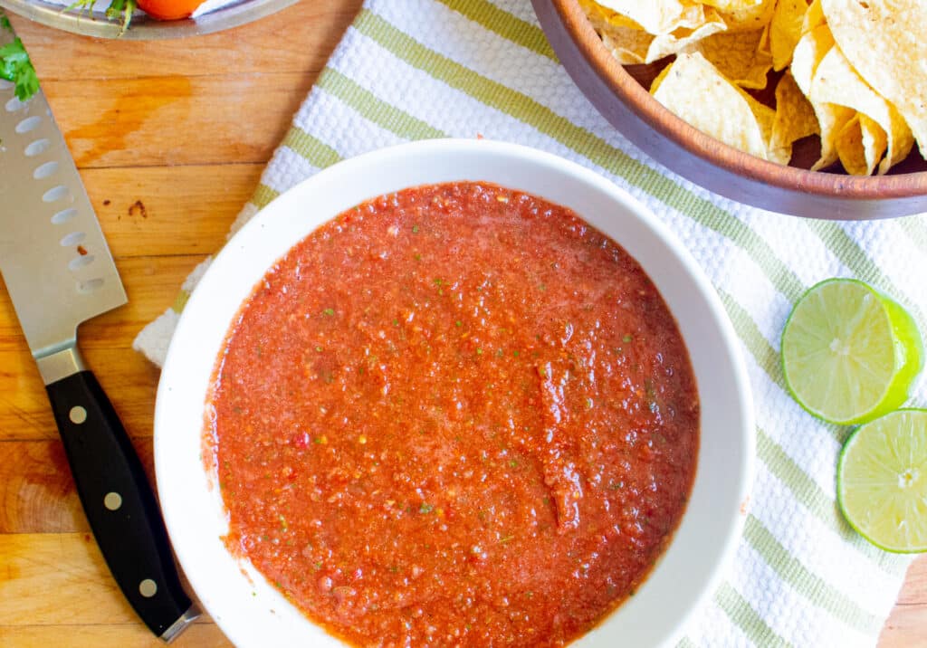 bowl of fresh homemade salsa with chips, lime, knife on a tea towel