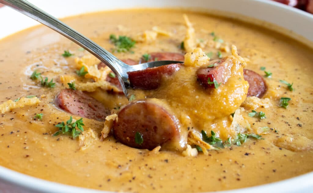 close up of sweet and savory roasted butternut squash soup with sausage and french fried onions in a white bowl on a spoon