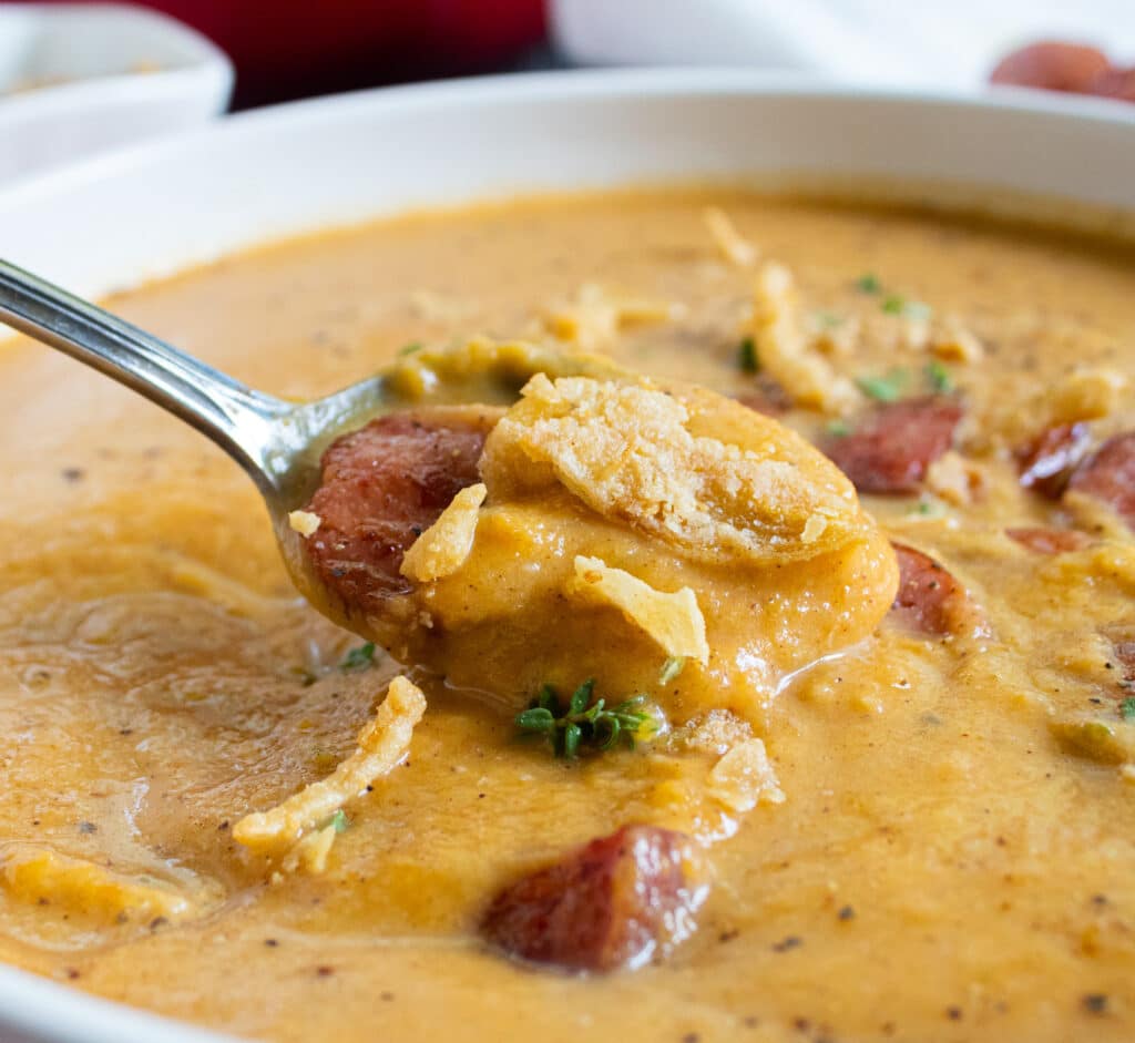 close up of sweet and savory roasted butternut squash soup with sausage and french fried onions on a spoon in a white bowl