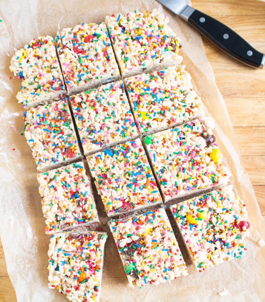 9x13 block of cut up rice krispie treats on parchment paper on a butcher block cutting board.