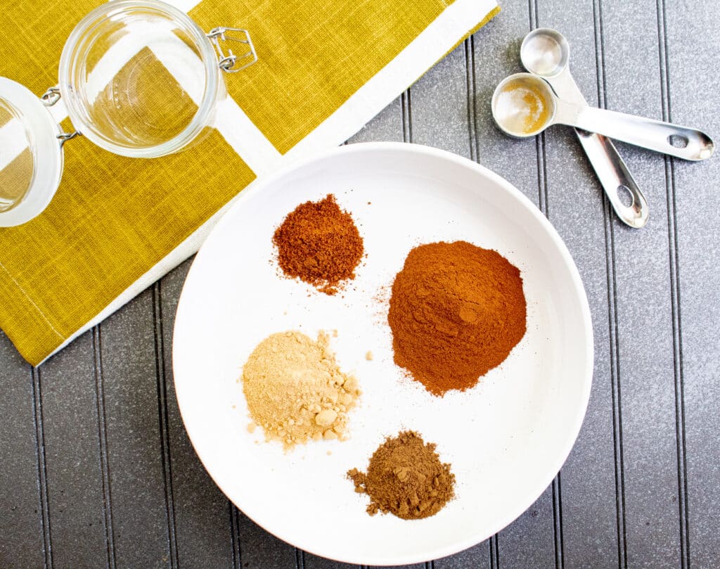 pumpkin pie spice ingredients on a white plate with measuring spoons and glass jar