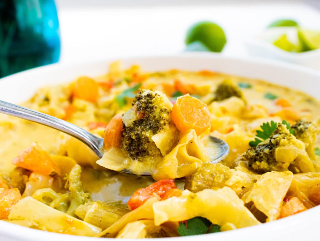 side close up of a bite of curry vegetable soup on a spoon.