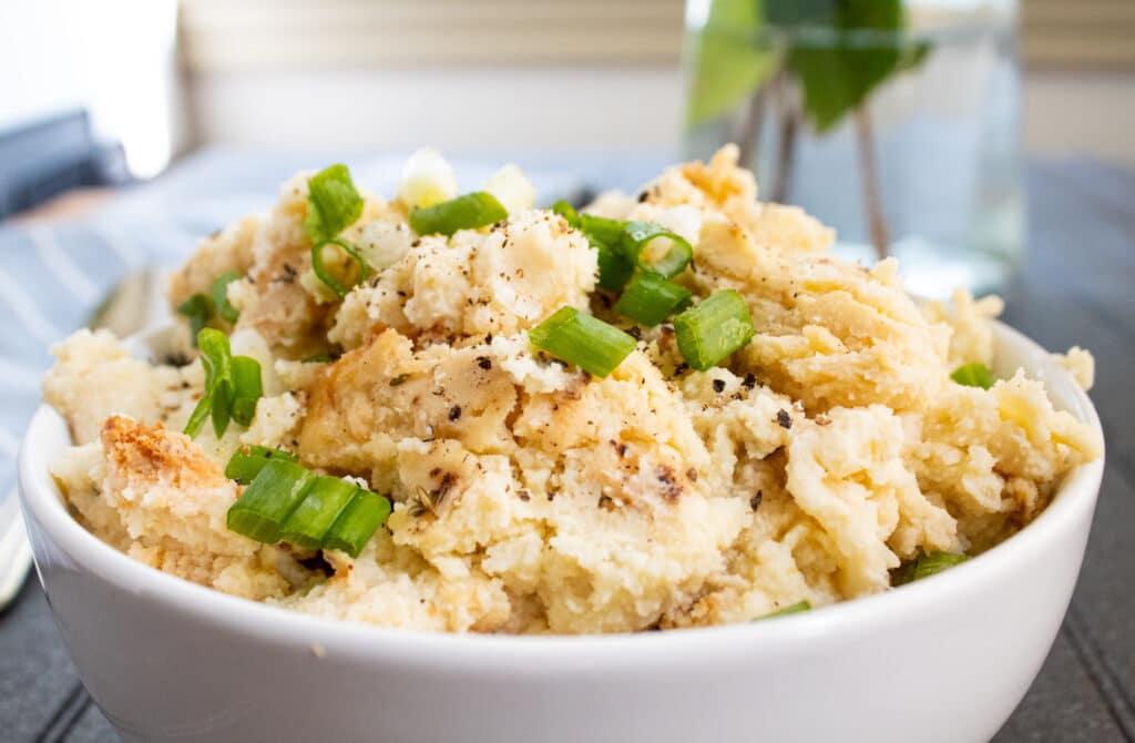 delicious comfort mashed potato cauliflower casserole in a white bowl with green onions