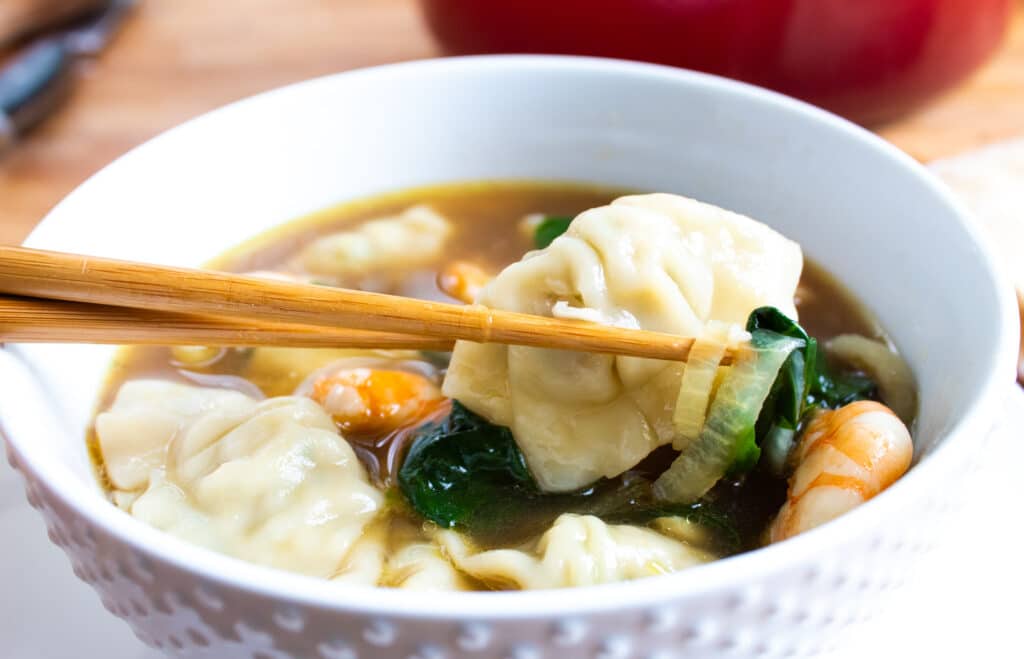 Close up of easy 30 minute wonton soup in a white bowl with chop sticks.