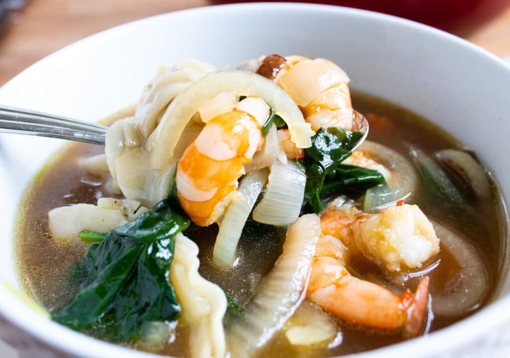 Close up of an individual bowl of wonton soup with shrimp and spinach.