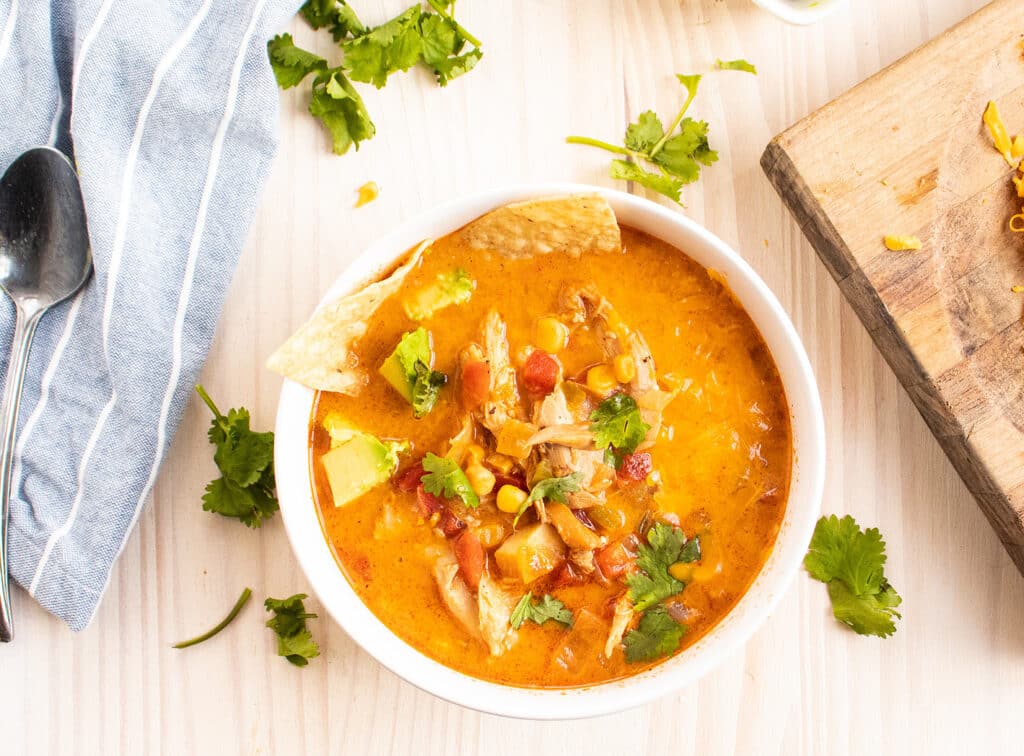 chicken tortilla soup in a white bowl with cilantro and chips