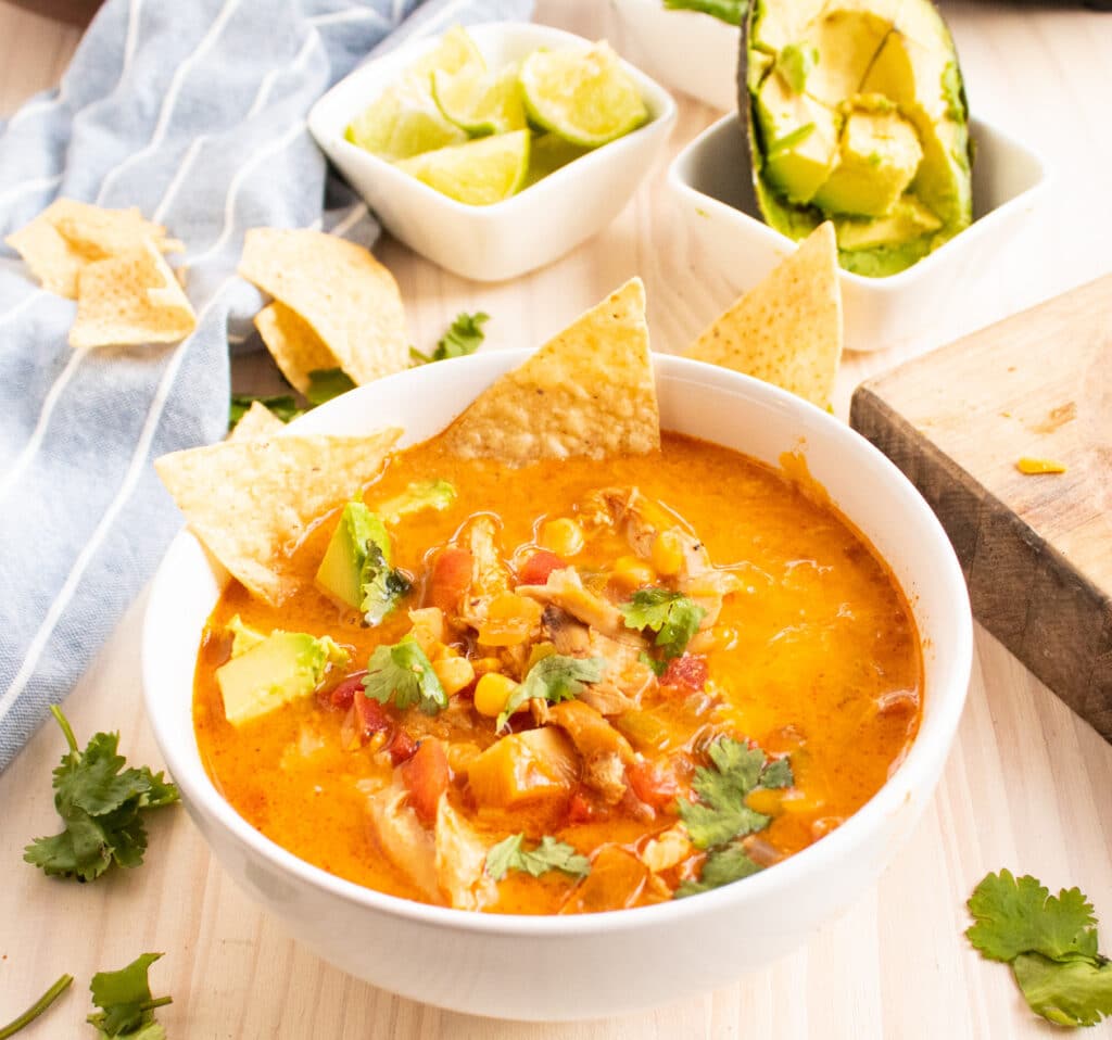 white bowl full of lower carb chicken tortilla soup with a few chips, avocado, and fresh cilantro