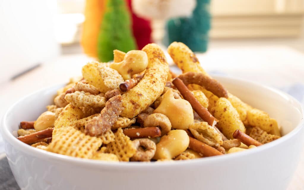 Closeup side view of curry cheese puff Chex mix in a white bowl..