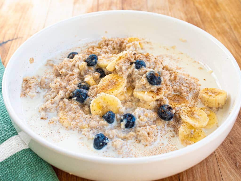 blueberry banana oatmeal breakfast in a white bowl on a butcher block table