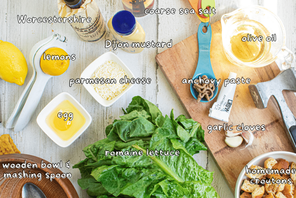 Caesar salad ingredients on a white wood table with labels for ingredients.