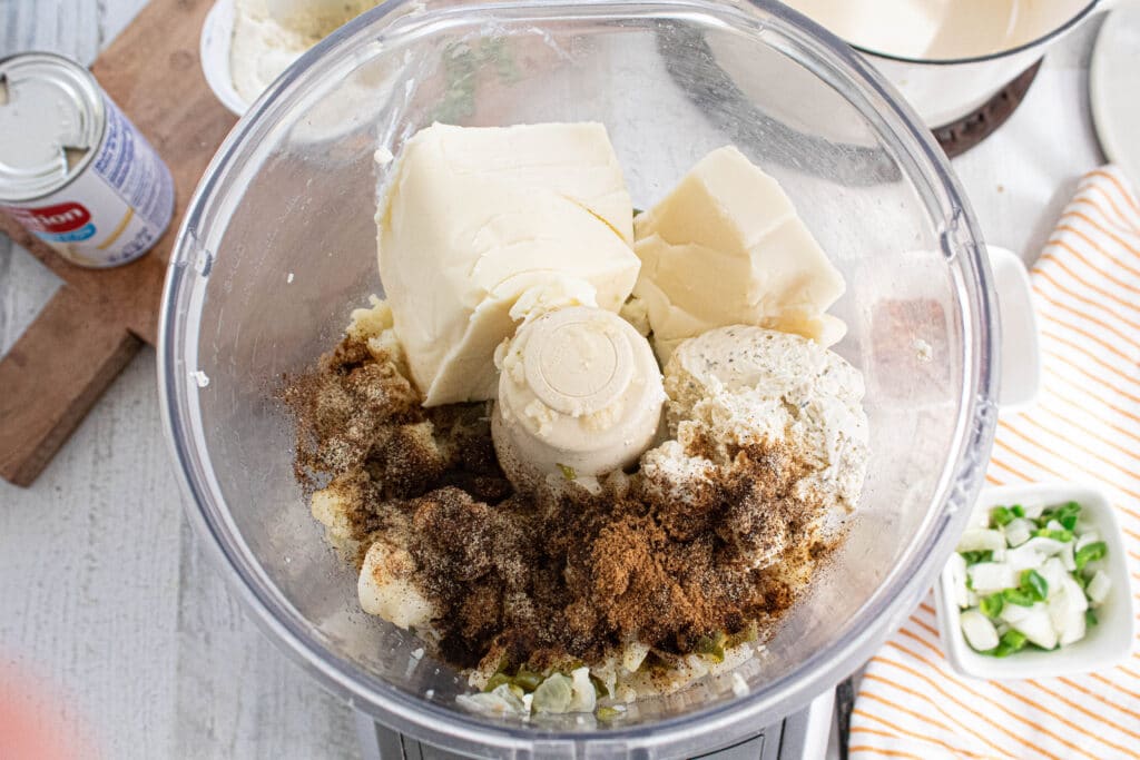 overhead pic of cheeses, cooked vegetables, and seasonings in a food processor.