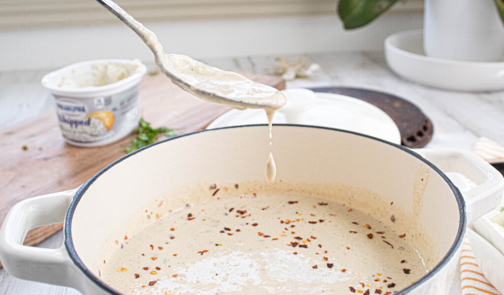 processed white cauliflower queso mixture in a white enameled cast iron stock pot with spoonful dripping.